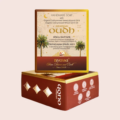 A boxed handmade soap product shown with the top package standing upright and the lower box lying beneath it on a plain light pink background. The packaging is primarily deep red/burgundy with gold accents and cream sections on the top label.