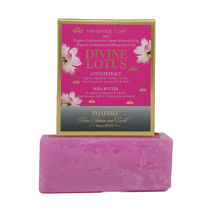 A pink bar of handmade Divine Lotus soap displayed in front of its pink and gold retail box, which features illustrations of lotus flowers and text detailing its ingredients and brand DYASSGA.