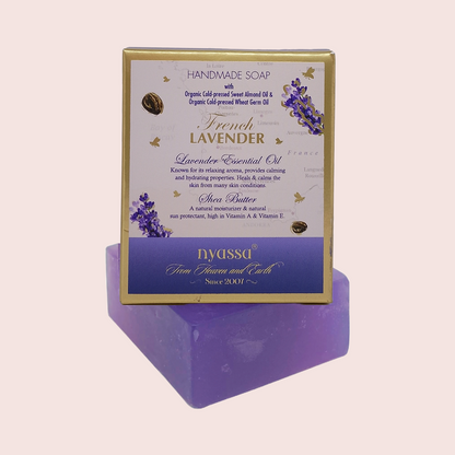 A boxed bar of handmade French Lavender soap displayed on top of a purple soap block. The packaging is cream and gold with purple lavender illustrations and the brand name 'Nyassu' visible on the lower section.