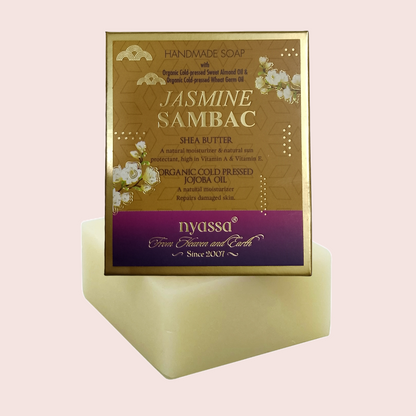 A handmade soap bar displayed on a matching rectangular pedestal, featuring a gold and purple label that reads 'JASMINE SAMBAC' and shows the brand 'nyassa'.