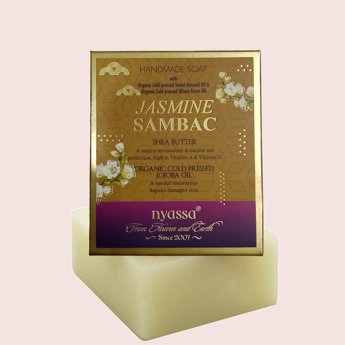Nyassa Jasmine Sambac handmade soap in a square gold-colored box with a purple brand banner, displayed on a pale yellow soap block against a light pink background.