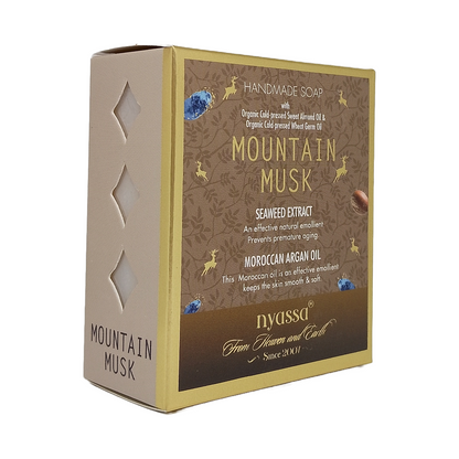 A boxed handmade soap product labeled 'Mountain Musk' by nyassa, shown on a plain white background. The package is a rectangular box with a beige side panel and a brown front label featuring gold text and decorative illustrations.
