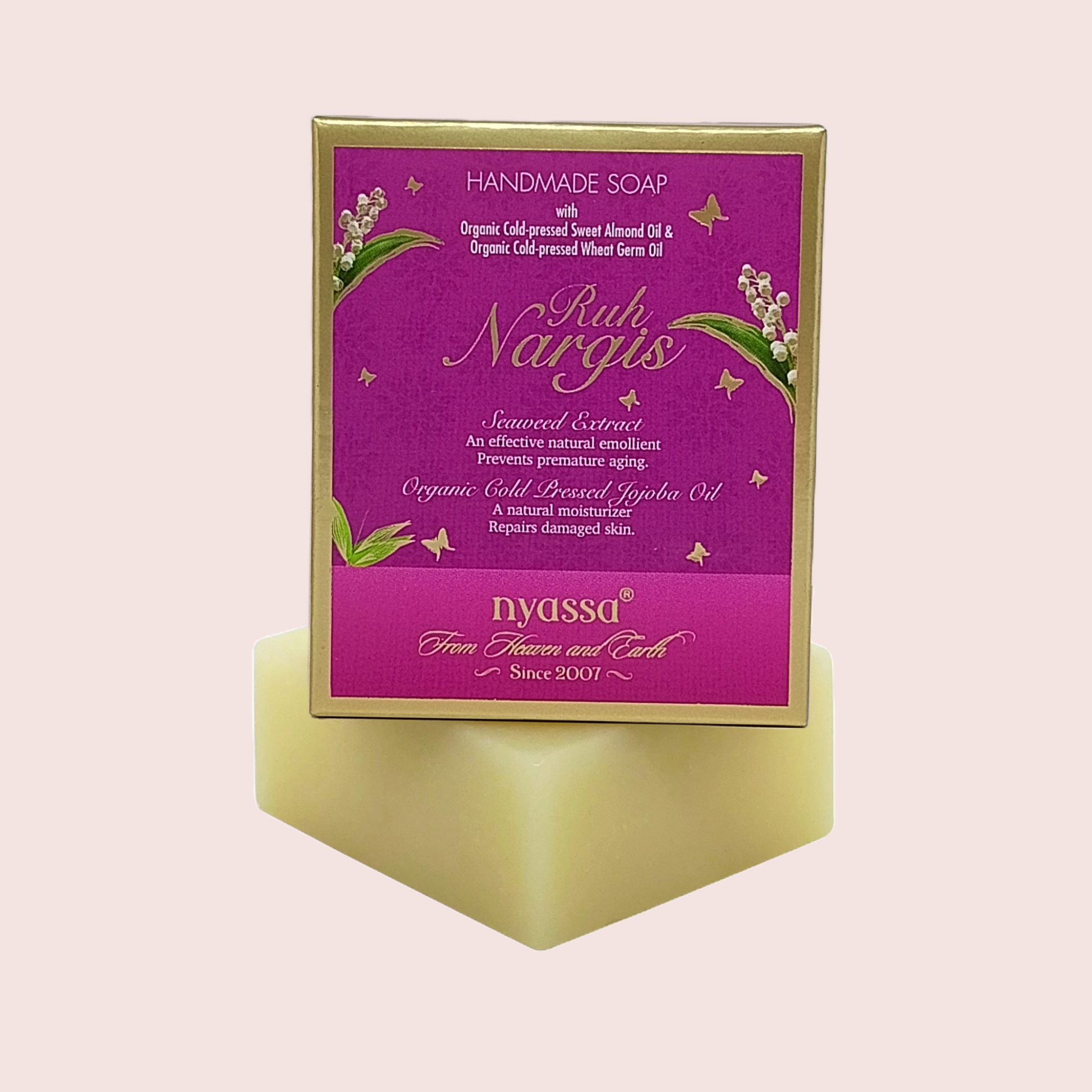 Nyassa Handmade Soap 'Rukh Nargis' in a purple and gold box, displayed on a pale yellow geometric stand against a light pink background.