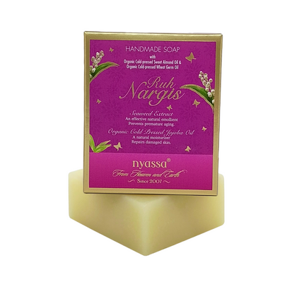 Nyassa Ruh Nargis handmade soap in a rectangular box with a magenta label and gold border, displayed on a gold-colored pedestal against a white background.