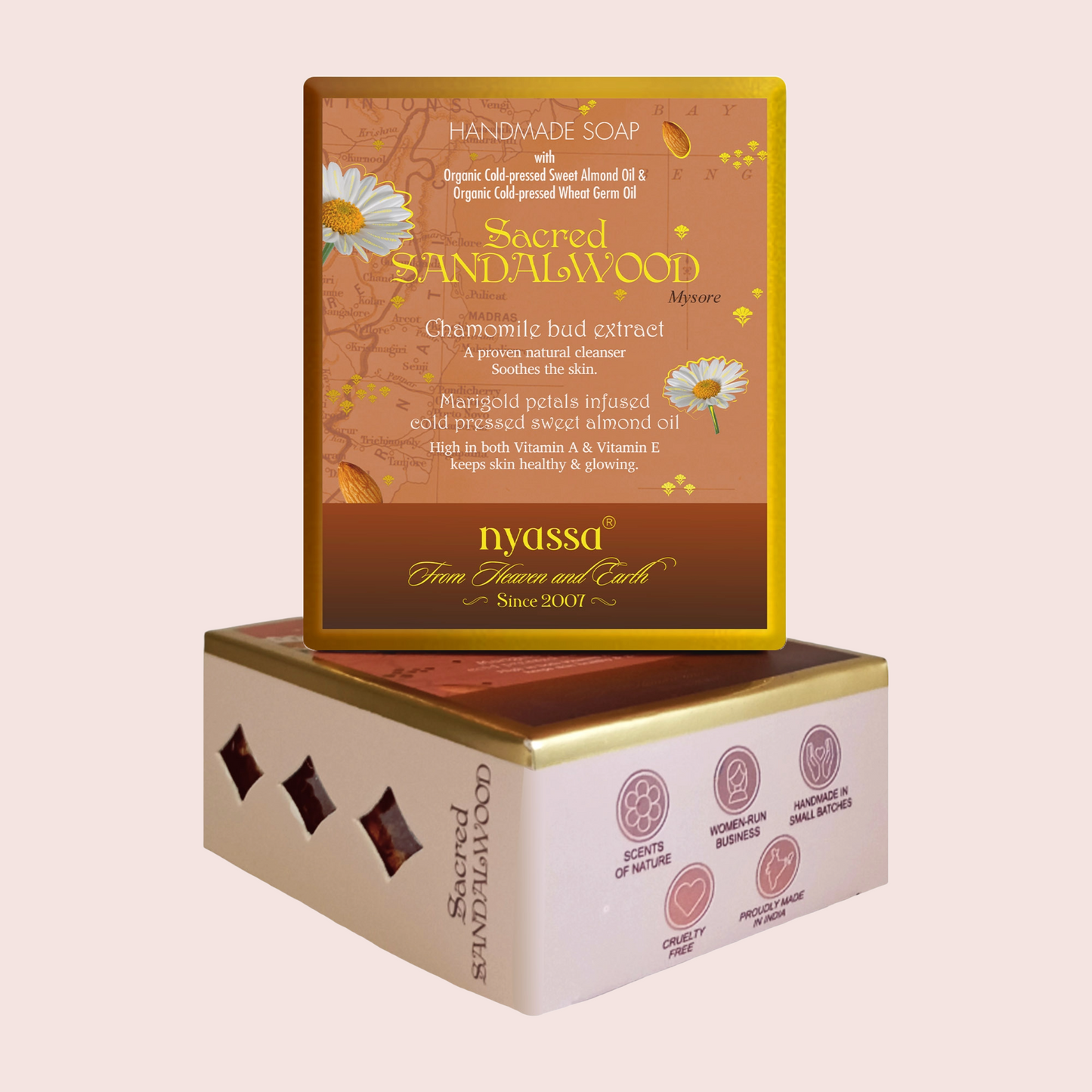 Nyassa Sacred Sandalwood Handmade Soap box packaging, featuring a brown and gold top lid with chamomile bud extract details, stacked on top of a cream-colored box with pink icons, set against a solid pale pink background.