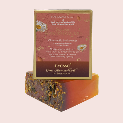 Nyassa Handmade Soap shown with its retail box. The soap bar is stacked on top of the box, displaying a marbled pattern of dark brown, orange, and yellow botanicals.