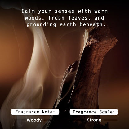 A dark, atmospheric fragrance graphic with a close-up of burning wood and smoke. White text at the top reads, 'Calm your senses with warm woods, fresh leaves, and grounding earth beneath.