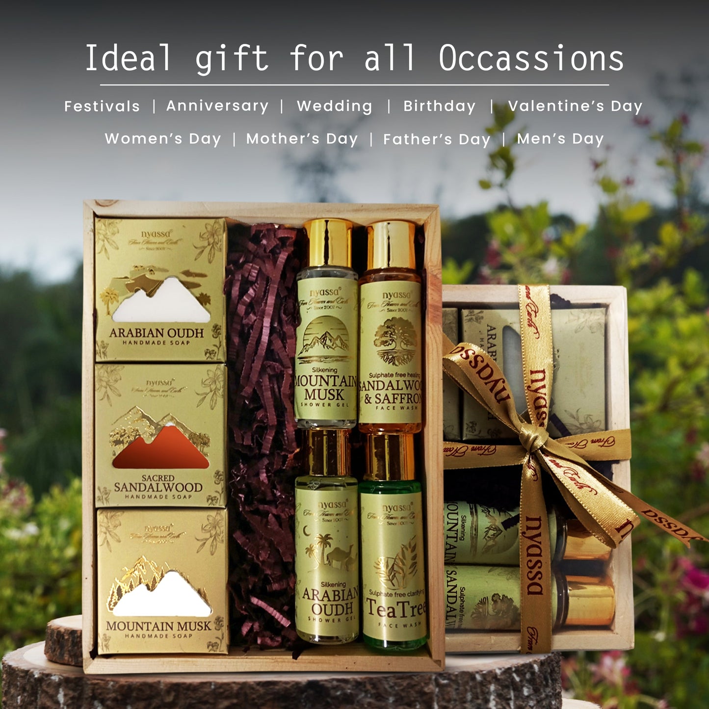 A boxed gift set of DSSDAU Arabian Oud and Mountain Musk handcrafted soaps and lotions, displayed on a tree stump with a blurred garden background. The set includes a wooden box with gold-patterned soaps, two tall bottles of Mountain Musk and Arabian Musk, and a smaller tea tree soap, tied with a gold ribbon.