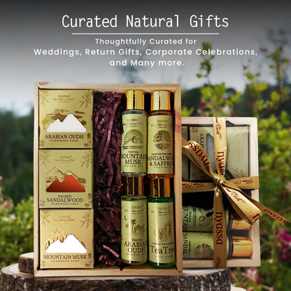 A curated gift set displayed in an open wooden box with a matching wrapped box beside it. The set includes boxed Arabian Oudh and Mountain Musk hand and body products, two Mountain Musk bottles, a Mountain Musk & Saffron body wash bottle, and a rolled Arabian Oudh bar tied with a branded ribbon.